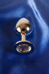 Metal sex toy butt plug on blue satin background